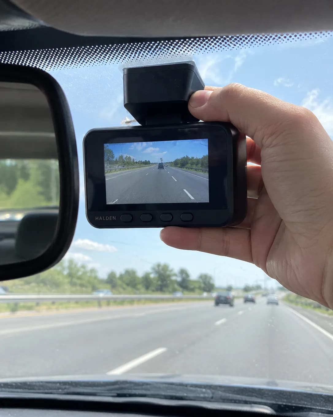 A hand pressing the Halden Duo 4K onto the windscreen behind the mirror