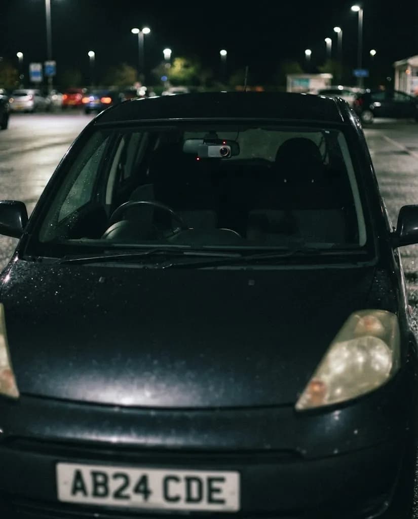 A car parked in a supermarket car park at night, the small Halden camera behind the mirror with its red recording light on