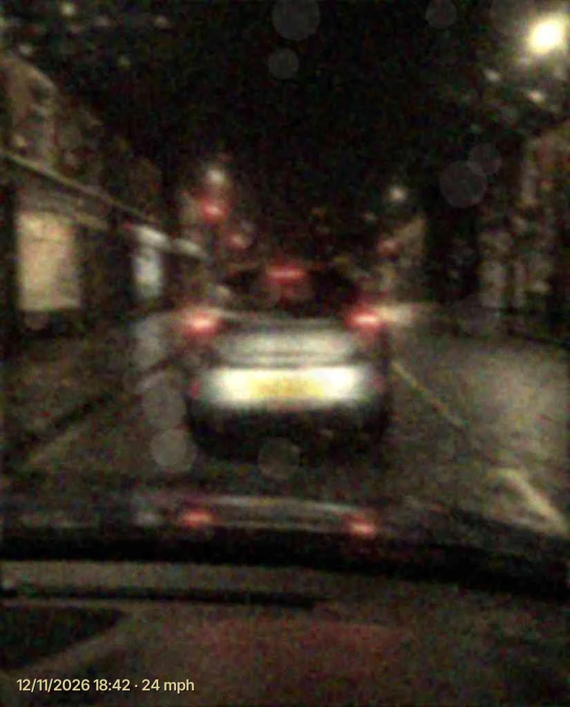 Night dash cam footage in the rain from a cheap camera, the plate of the car ahead a blur